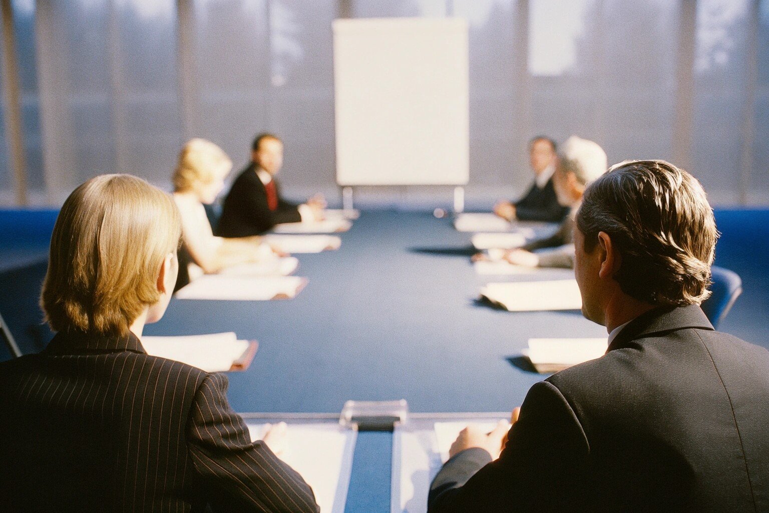 A workshop group around a boardroom table, facing an empty flipchart