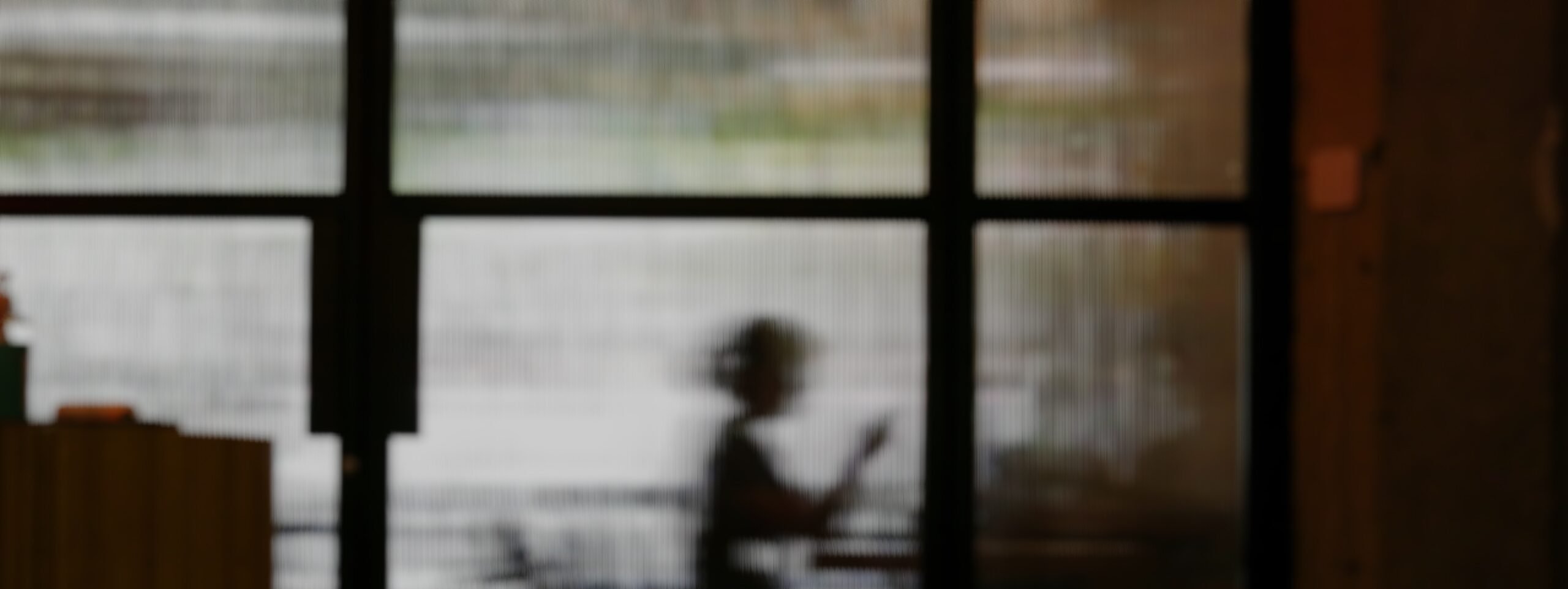 A silhouette at a desk seen through a rain-streaked studio window